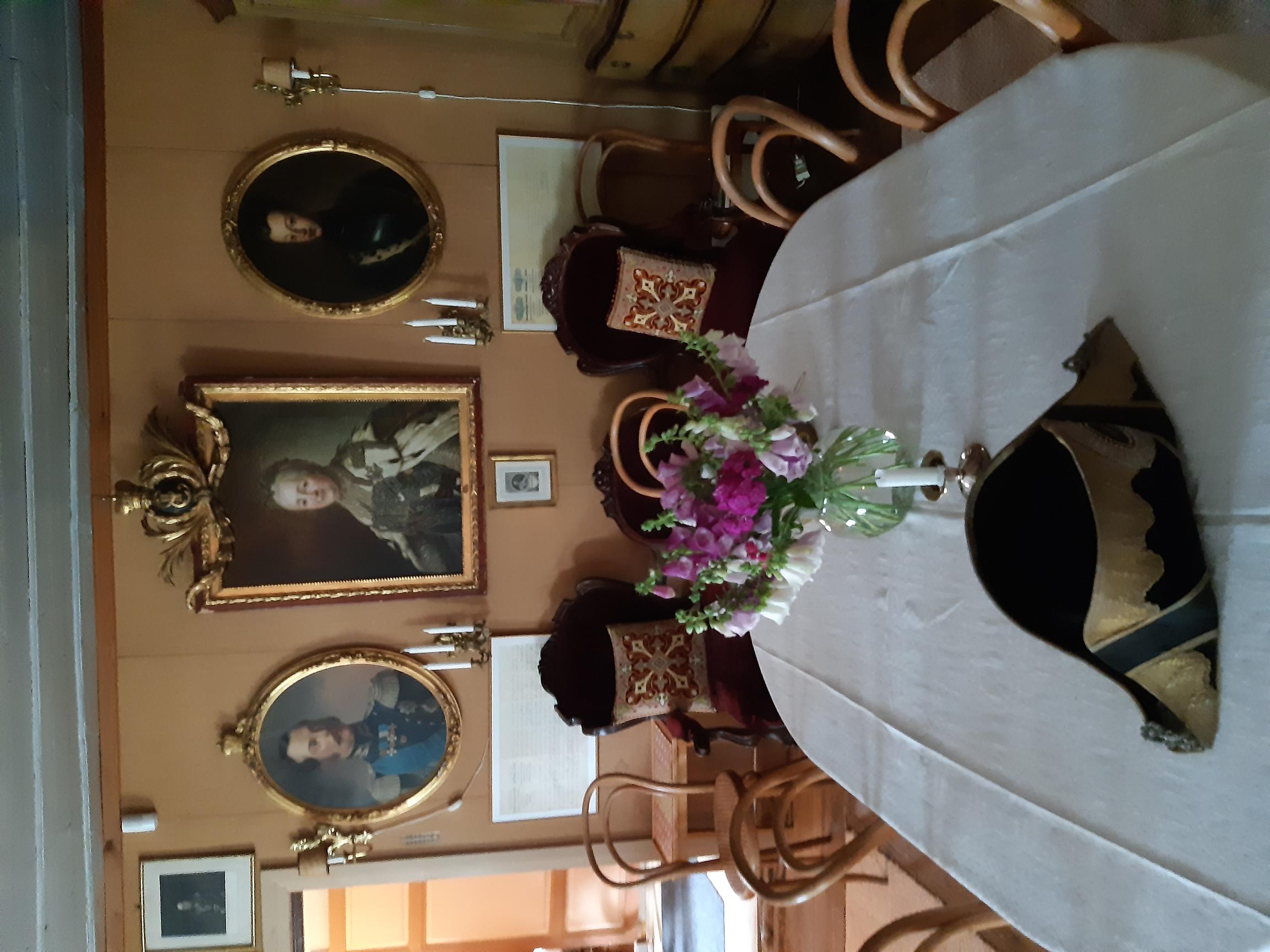 Kuvassa näkyy Mäntyniemen kartanon sali, jossa muotokuvatauluja seinällä sekä iso pöytä tuolit ympärillään.