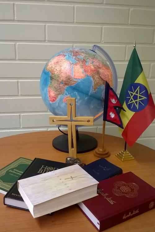 Pöydällä maapallo ja risti ja kaksi lippua.  Pöydällä lisäksi Raamattuja eri kielillä.